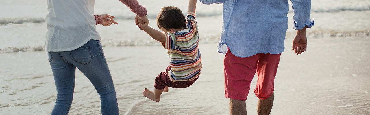 child swinging between parents hands, jumping waves on the beach